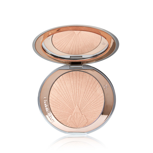 An open, pressed powder highlighter compact in a light pinky beige shade with a mirrored lid. 