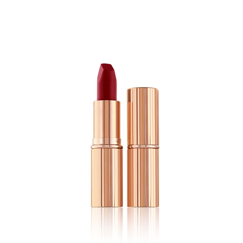 Two lipsticks, one with its lids and the other without, in a true ruby red matte shade with golden-coloured packaging. 