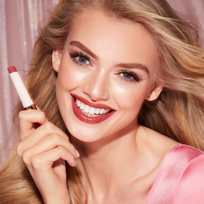 Hyaluronic Happikiss in Passion Kiss on fair-tone model Fair-tone model with blue eyes wearing a moisturising lipstick balm in a soft brown shade with a high-shine finish while holding the lip balm.