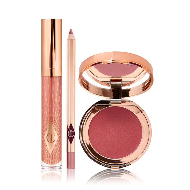A nude pink lip gloss in a glass tube with a gold-coloured lid with a nude pink lip liner pencil, and an open, mirrored-lid lip and cheek cream compact in a berry-red shade. 