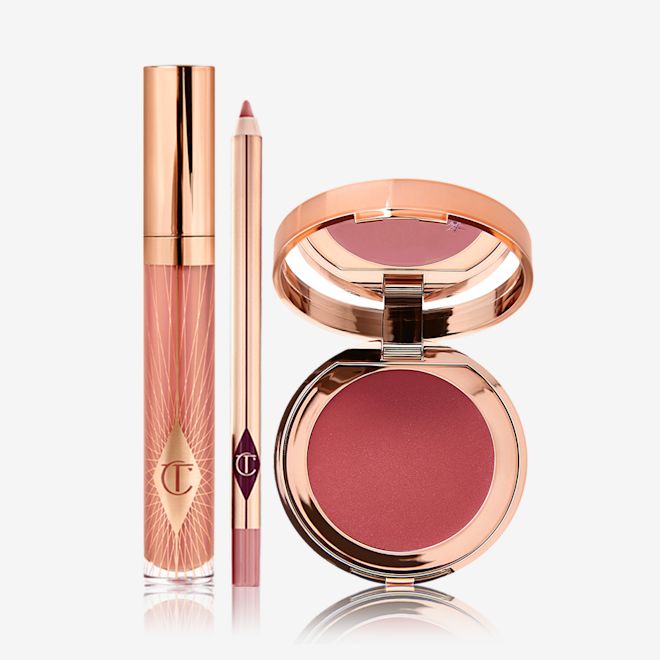 Pillow Talk Just Kisses Glow Kit displayed A nude pink lip gloss in a glass tube with a gold-coloured lid with a nude pink lip liner pencil, and an open, mirrored-lid lip and cheek cream compact in a berry-red shade.