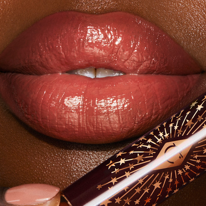 Lips close-up of a deep-tone model wearing a glossy soft coral lipstick lip balm. 