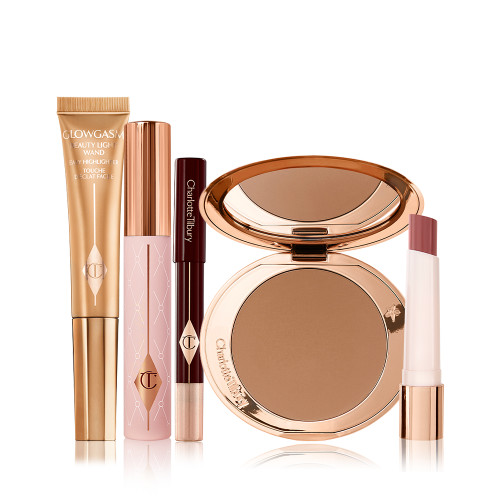 Liquid highlighter wand in a honey gold shade, mascara in a nude pink tube with a gold-coloured lid, chubby eyeshadow stick in a champagne shade, bronzer compact with a mirrored-lid in a dark brown shade, and lipstick balm in a nude berry red shade.