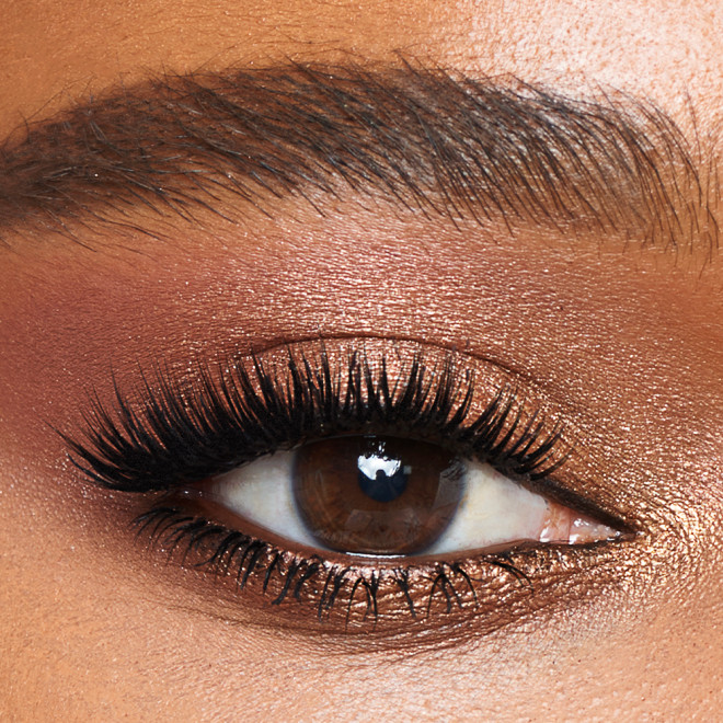 Single-eye close-up of a deep-tone model with brown eyes wearing metallic honey gold, soft amber, and dark chocolate brown eye makeup. 