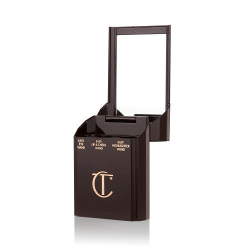 An open, black-brown-coloured portable makeup case with a mirrored lid, with three product places, which are for eyeshadow stick, lip and cheek stick, and highlighter stick.