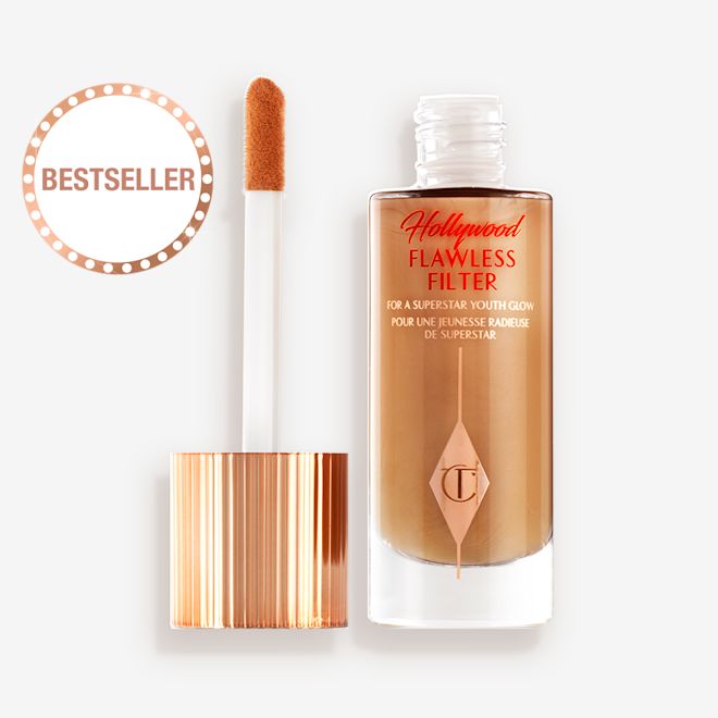 HFF-6.5-LEGENDARY-PDP 1 An open, luminous primer in a dark golden-beige shade in a glass bottle with its gold and white doe-foot applicator next to it.