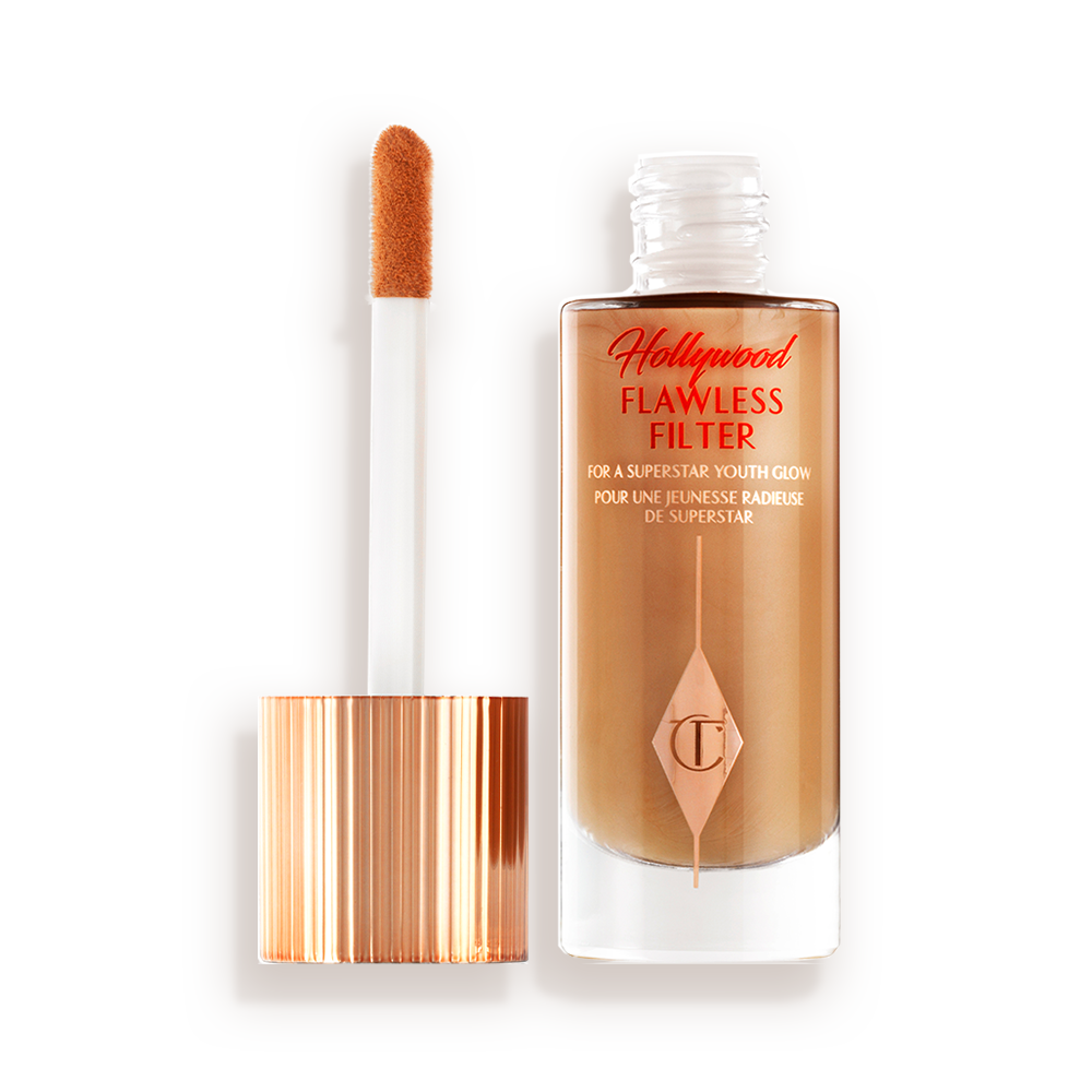 Ein leuchtender Primer in einem dunklen Gold-Beigeton in einer geöffneten Glasflasche mit seinem angeschrägten Applikator in Gold und Weiß neben sich.