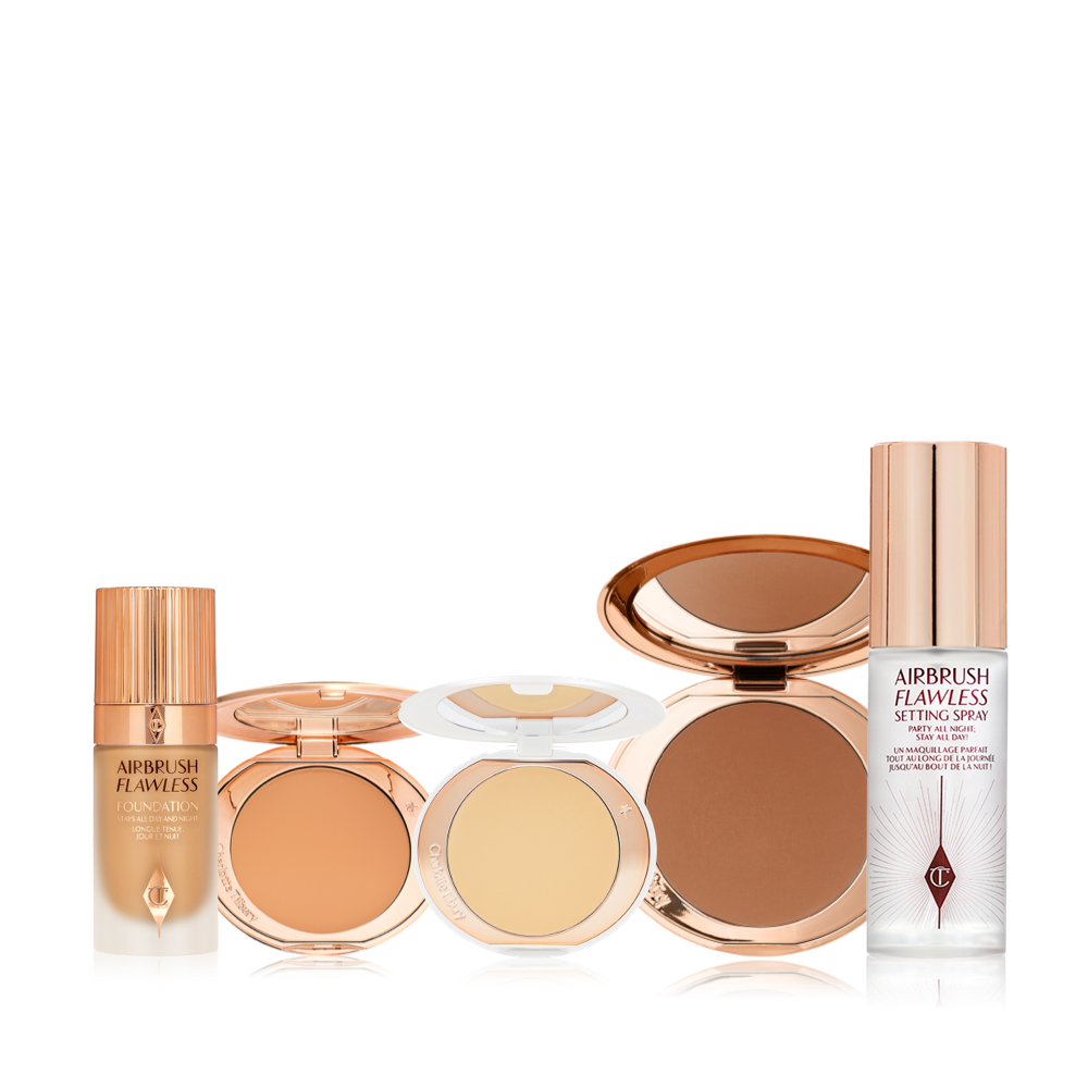Foundation in a glass bottle with a gold-coloured lid, pressed powder and powder bronzer compacts, cream bronzer compact, and setting spray in a large, clear bottle with a gold-coloured lid.