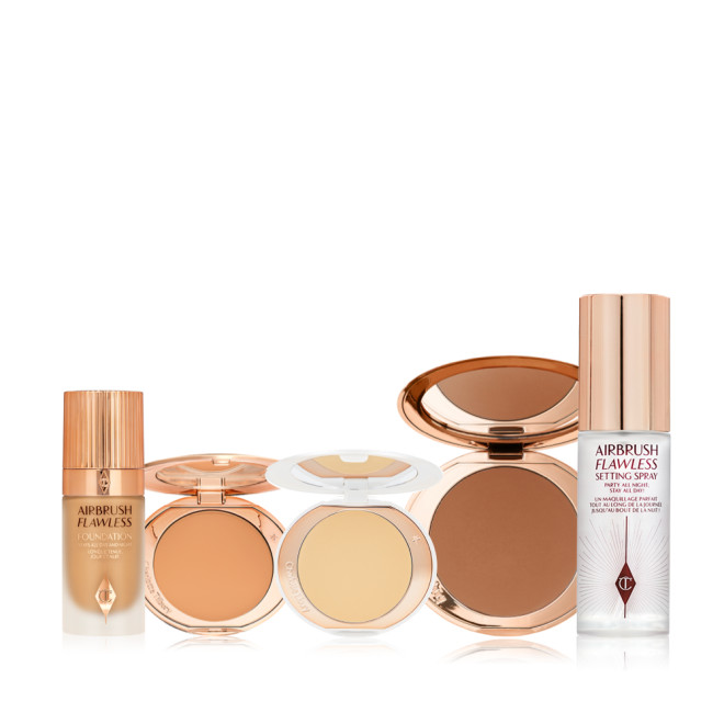 Foundation in a glass bottle with a gold-coloured lid, pressed powder and powder bronzer compacts, cream bronzer compact, and setting spray in a large, clear bottle with a gold-coloured lid.