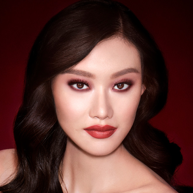A fair-tone brunette model with reddish-plum eye makeup, glowy face base, and a vampy-red lipstick with a satin-finish. 