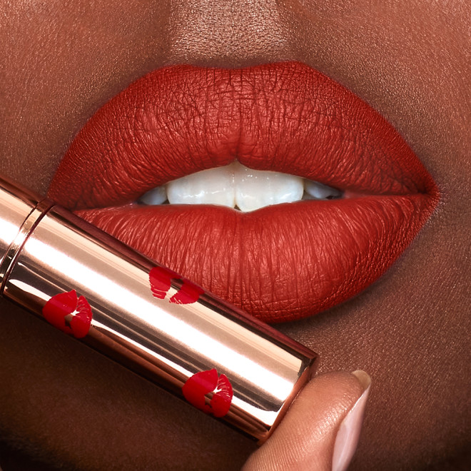 Lips close-up of a medium-tone model wearing tawny orange-red lipstick with a matte finish.