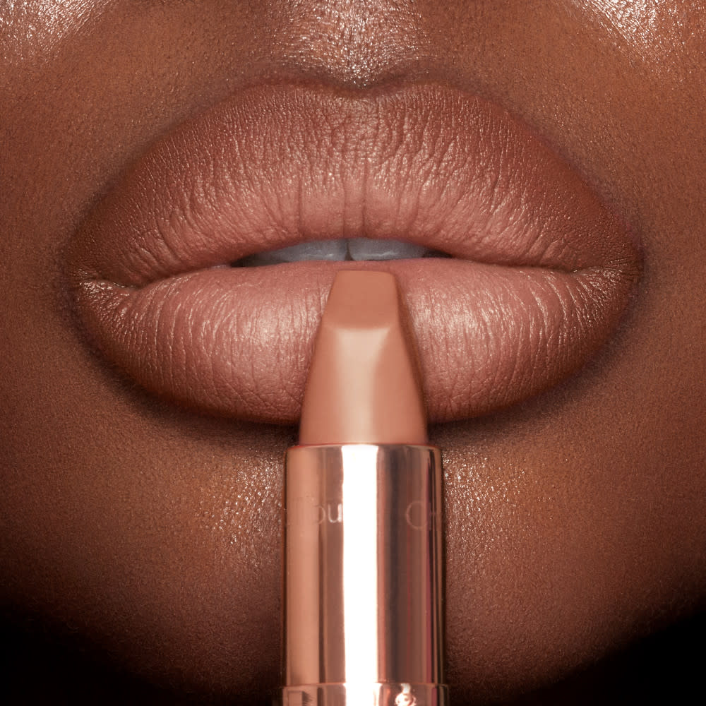 Lips close-up of a deep-tone model applying a muted apricot lipstick with a matte finish.