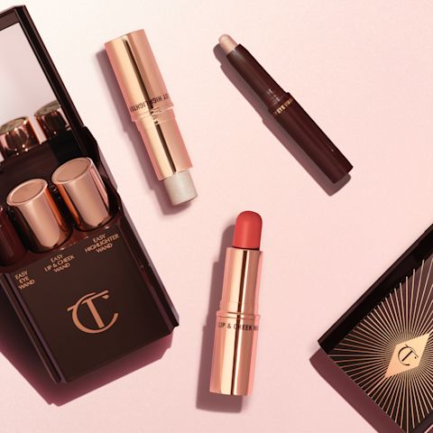 Open makeup kits with mirrored lids with products inside them displayed: a lip and cheek wand, highlighter stick, and eyeshadow stick, and the three products placed outside of the kit.