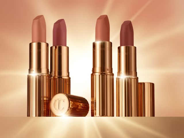 Four open lipsticks in gold-coloured tubes in nude shades of rose-brown, peach, apricot, and pink.