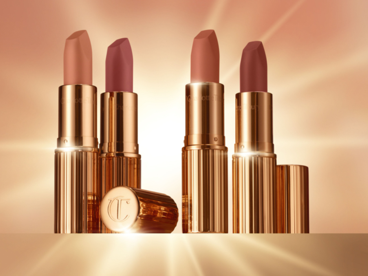 Four open lipsticks in gold-coloured tubes in nude shades of rose-brown, peach, apricot, and pink.