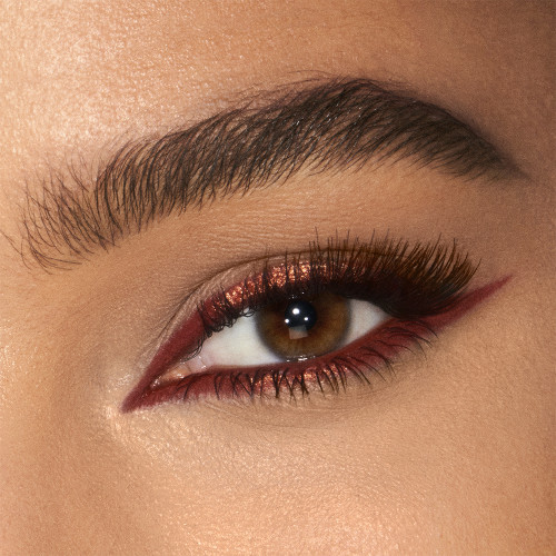 Eye close-up of a tanned model wearing a glistening, coppery-rust-coloured eyeliner on the upper lid and lower waterline.