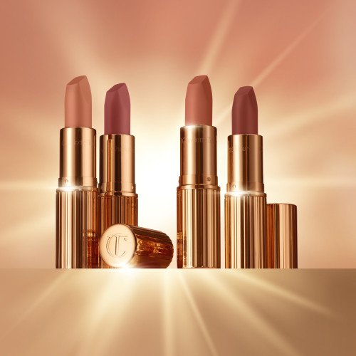 Four open lipsticks in gold-coloured tubes in nude shades of rose-brown, peach, apricot, and pink.