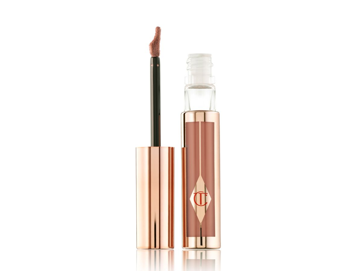 A lip gloss in a warm brown shade with red undertones in a clear tube with golden design with its doe-foot applicator next to it. 