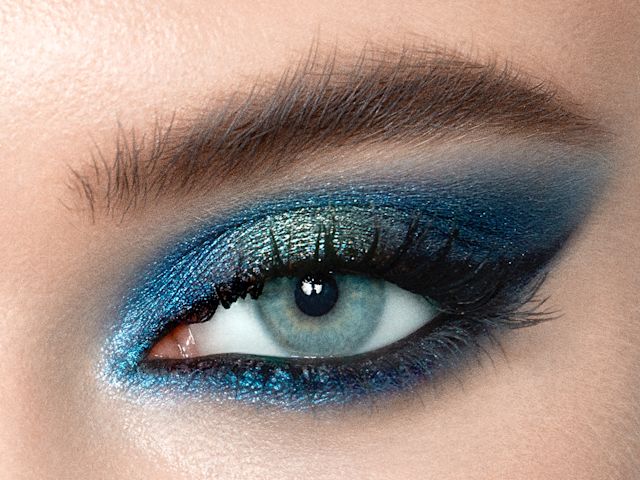 Close-up of a light-tone model's blue eye with shimmery, teal, royal blue, and ice blue eye makeup. 