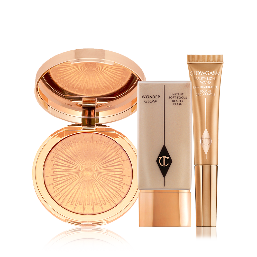 An open, mirrored-lid highlighter compact in a soft gold shade, glowy primer in a rectangular, transparent bottle with a gold-coloured lid, and a highlighter wand in a honey-gold shade.