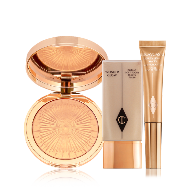 An open, mirrored-lid highlighter compact in a soft gold shade, glowy primer in a rectangular, transparent bottle with a gold-coloured lid, and a highlighter wand in a honey-gold shade.