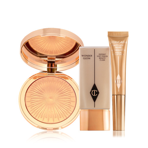 An open, mirrored-lid highlighter compact in a soft gold shade, glowy primer in a rectangular, transparent bottle with a gold-coloured lid, and a highlighter wand in a honey-gold shade.
