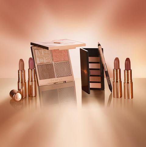 Banner with four, open lipsticks in nude shades of pink and brown, an open highlighter and blush palette with glowy gold and nude brown and peach shades, a 6-pan eyeshadow palette with nude brown, peach, and black shades, and a double-ended eyeliner pen in beige and black colour.