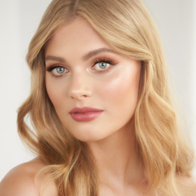 A fair-tone model with blue eyes wearing a matte lipstick in a  delicate rose-bud pink hue. 
