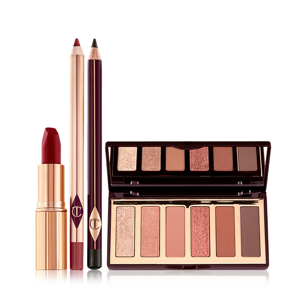 An open, matte lipstick in a dark red shade in a gold-coloured tube, open lip liner pencil in a redwood shade, eyeliner pencil in dark brown, and an open, mirrored lid eyeshadow palette with six eyeshadows in shades of peach, gold, pink, and brown.