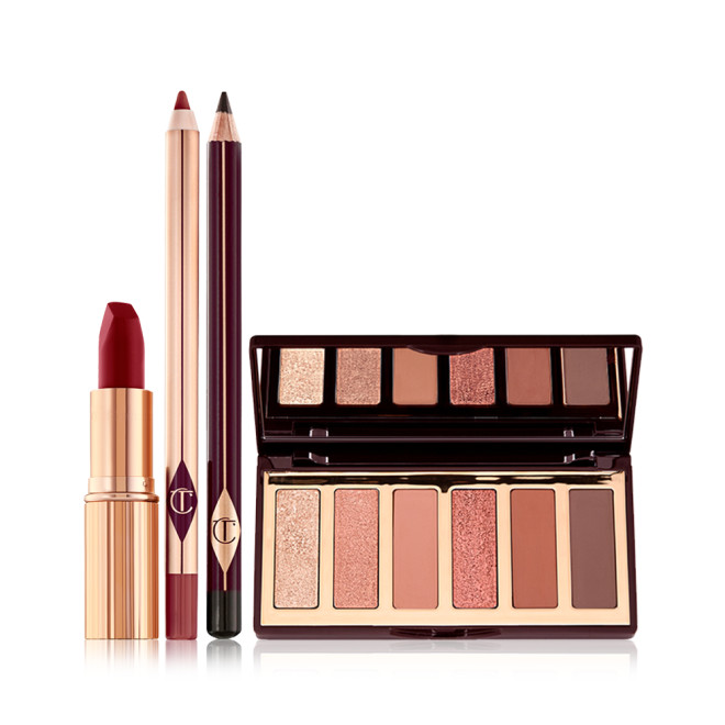 An open, matte lipstick in a dark red shade in a gold-coloured tube, open lip liner pencil in a redwood shade, eyeliner pencil in dark brown, and an open, mirrored lid eyeshadow palette with six eyeshadows in shades of peach, gold, pink, and brown.