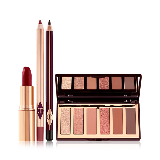 An open, matte lipstick in a dark red shade in a gold-coloured tube, open lip liner pencil in a redwood shade, eyeliner pencil in dark brown, and an open, mirrored lid eyeshadow palette with six eyeshadows in shades of peach, gold, pink, and brown.