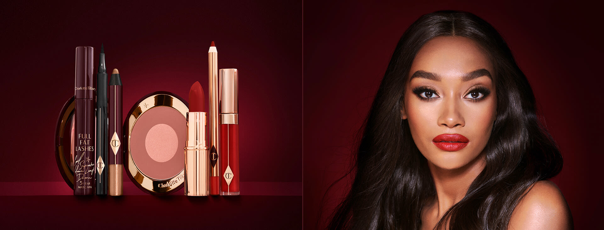 A deep-tone model with brown eyes wearing shimmery bronze eye makeup with muted pink blush and glossy scarlet-red lips, along with an open two-tone blush in cool-toned terracotta and warm pink with a mascara, eyeliner pen, an open lipstick in bold red, lip liner pencil in blood-red, and a lip gloss in bright red. 