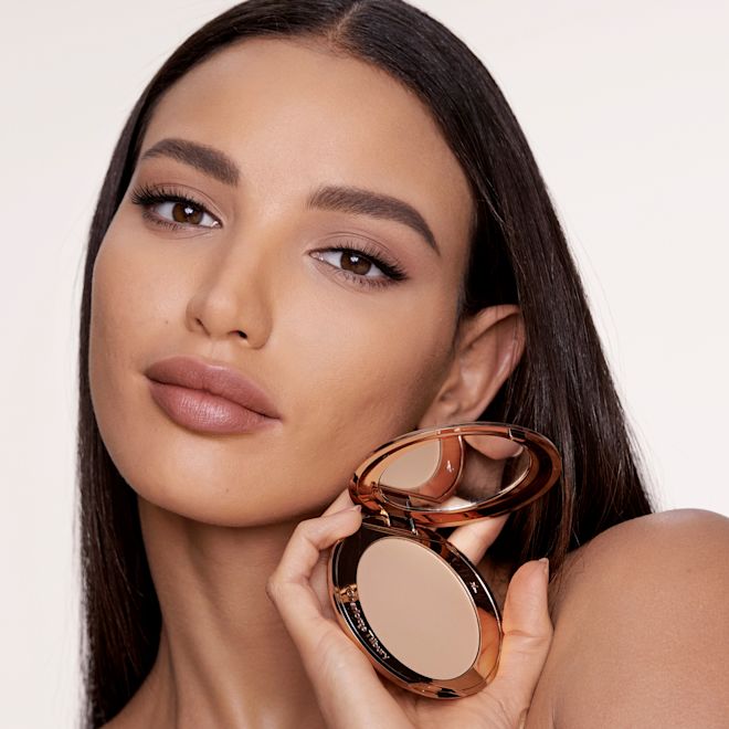 Makeup Starter Kit in Medium on medium-tone model Medium-tone brunette model with flawless, matte skin wearing a nude pink lipstick and holding an open, pressed powder compact in a medium shade.