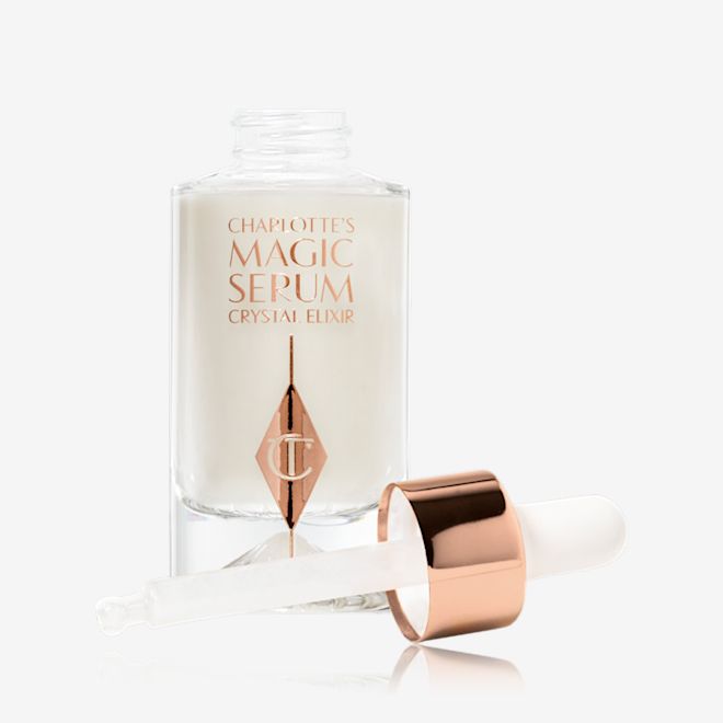 Charlotte's Magic Serum Crystal Elixir Open A pearly-white serum in a glass bottle with its dropper applicator next to it.