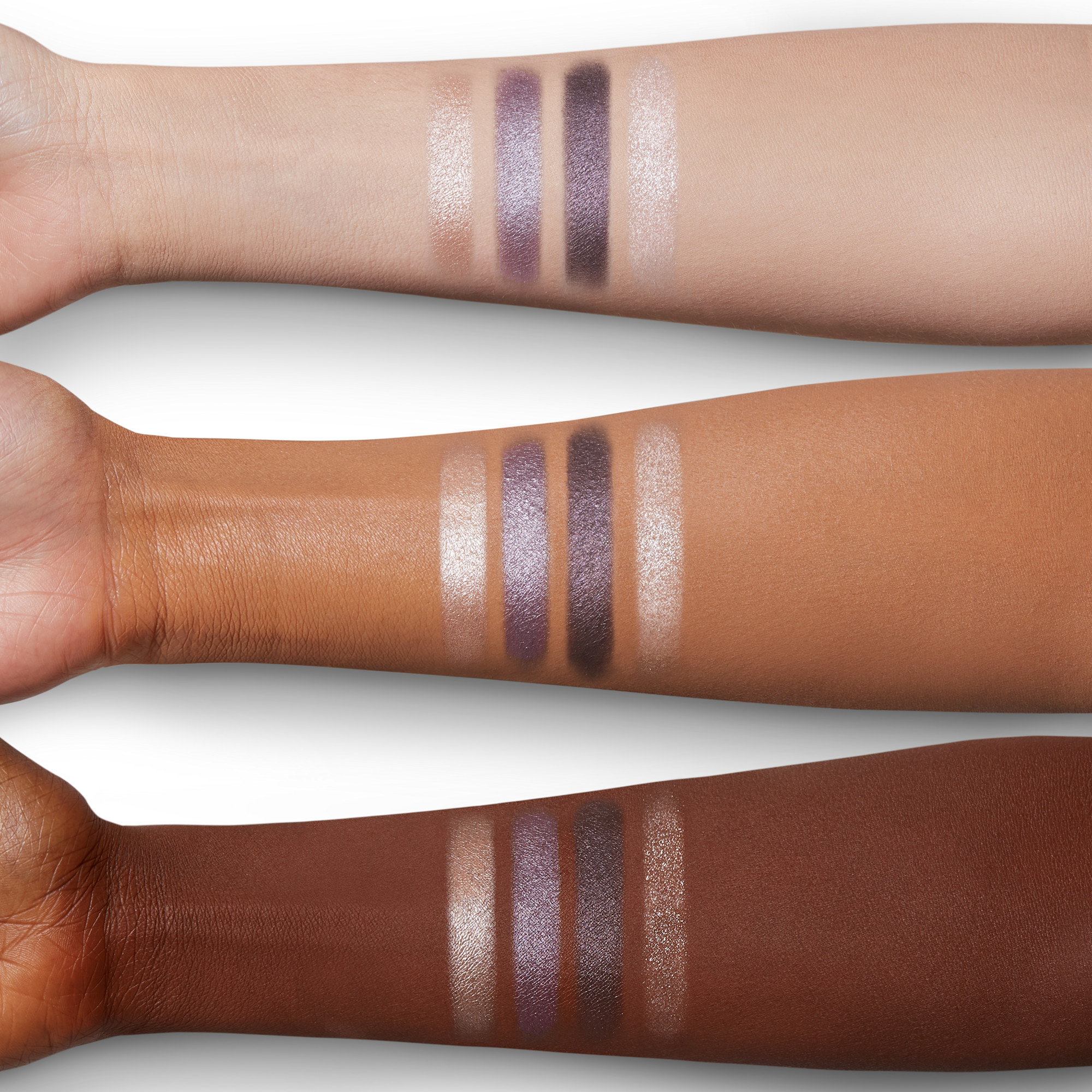 Arm swatches of four shimmery eyeshadows in champagne, blush pink, and smokey grey colours on fair, tan, and deep skin. 