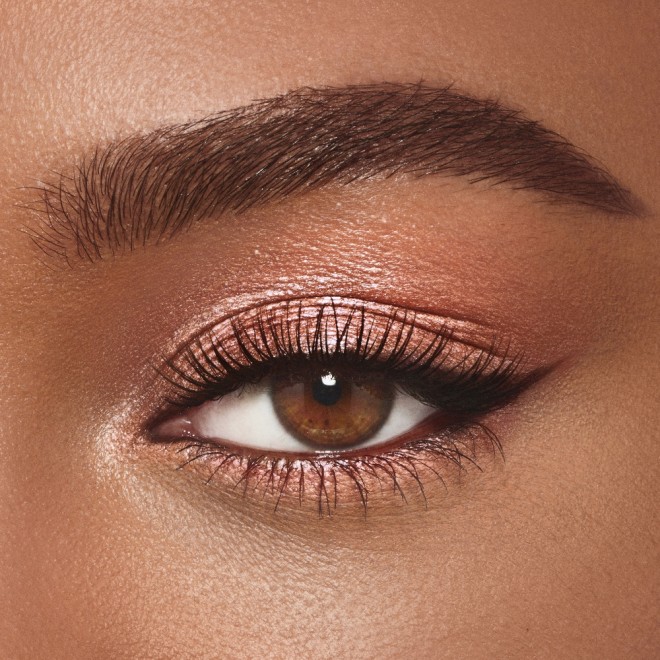 Single-eye close-up of a deep-tone model with brown eyes wearing a shimmering nude cream eyeshadow.