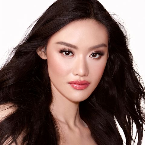 A fair-tone model with brown eyes wearing shimmery rose gold and brown eye makeup with brown eyeliner, soft pink blush, and coral-pink lipstick with gloss on top. 