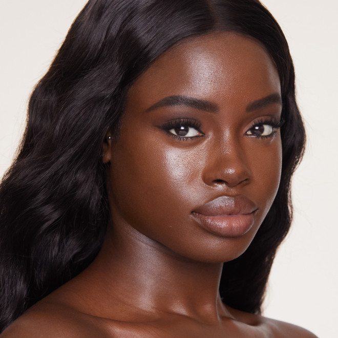 Deep-tone brunette model wearing glowy foundation in a dark brown shade that covers her pores and makes her skin look flawless and youthful.