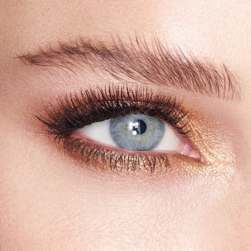 Single-eye close-up of a model with blue eyes wearing cream eyeshadow in a rich, burnished, amber-gold shade.