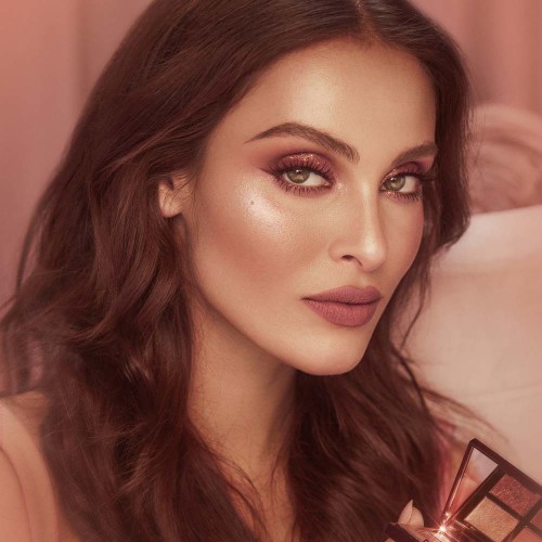 Medium-tone brunette model wearing berry-rose matte lipstick with nude pink highlighter blush, and shimmery rose gold eye makeup with black eyeliner. 