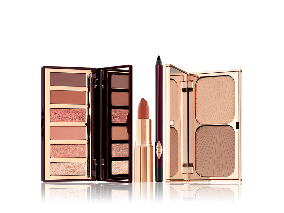 An open, mirrored-lid eyeshadow palette with eyeshadows in shades of brown, pink, and golden, an open lipstick in dark coral shade, eyeliner pencil in black, and duo contour palette with a mirrored lid. 