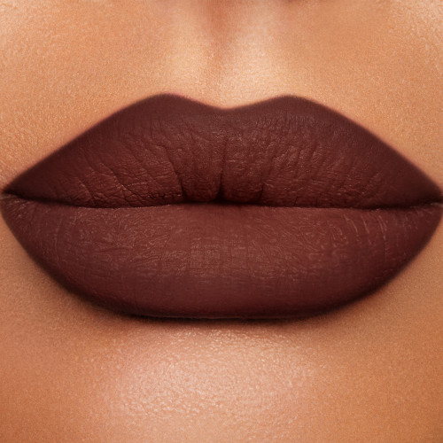 Close-up of a tanned model's lips that have a tawny-brown matte lip shade applied to them.