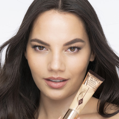 Medium-light-tone brunette model wearing glowy, skin-like foundation with a satin finish with nude lipstick and subtle eye makeup.