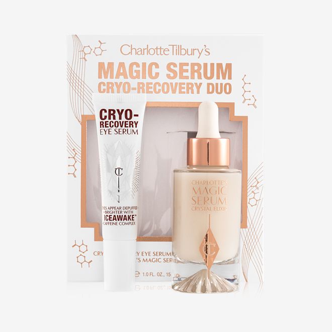 Cryo-Recovery Eye Serum and Magic serum with box Eye serum in a white-coloured tube with geometric patterns on the front in a reflective, silver colour along with luminous, facial serum in a glass bottle with a white and gold dropper lid with their packaging box behind them.