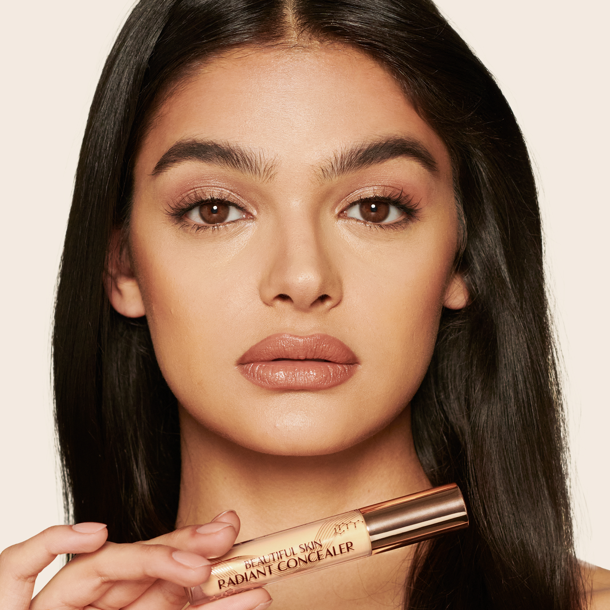 Medium-tone model with brown eyes wearing a radiant, concealer that brightens, covers blemishes, and makes her skin look fresh along with nude lip gloss and subtle eye makeup.