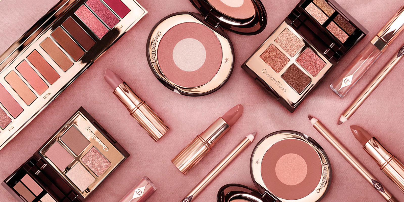 An array of make-up products, all open, include two-tone blushes, nude-pink and berry-pink lipsticks and lip liner pencils, lip glosses, and eyeshadow palettes with mirrored lids. 
