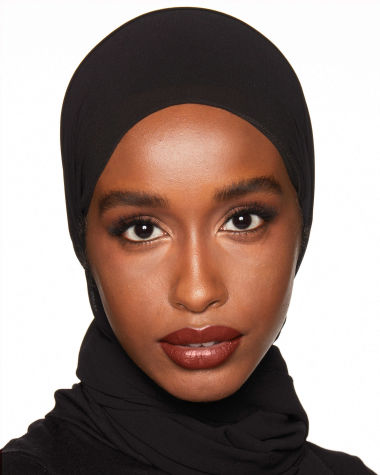 Deep-tone model with brown eyes wearing a moisturising lipstick balm in a soft brown shade with a high-shine finish.