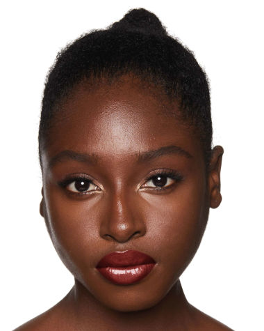 Deep-tone model with brown eyes wearing a moisturising lipstick balm in a berry shade with a high-shine finish.