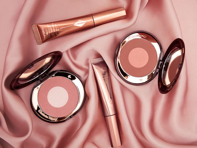 Two, open, mirrored-lid, two-tone powder blushes and two, glowy blush wands placed on a nude-pink, satin sheet. 