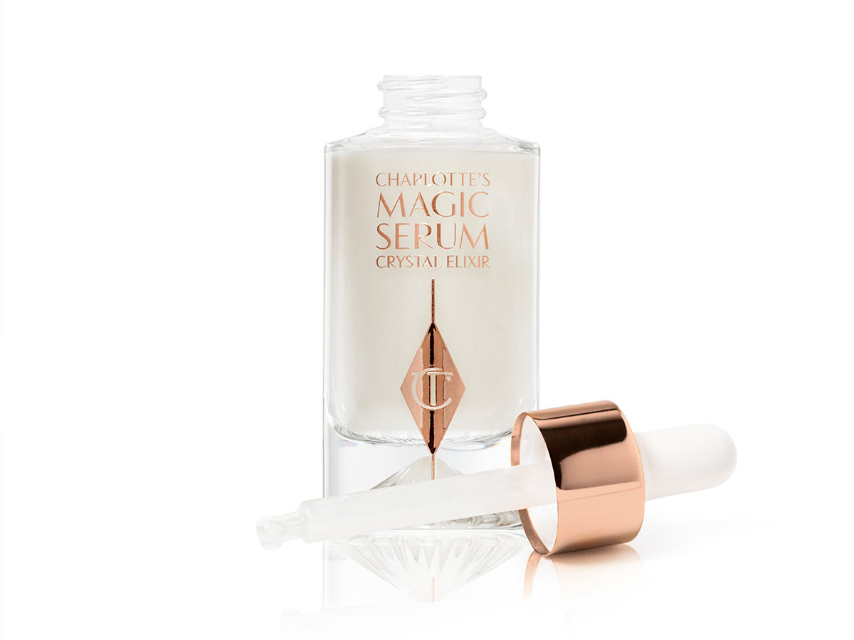 An open luminous, ivory-coloured serum in an opened glass bottle with its dropper beside it. 